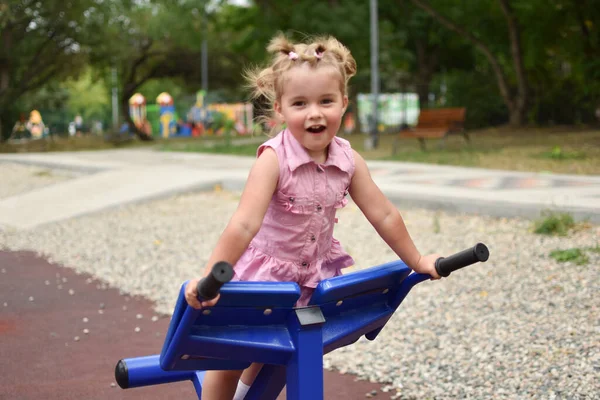 Grappig klein meisje in een roze jurk op de outdoor sport simulator. — Stockfoto