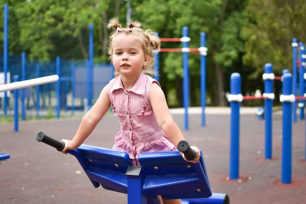 Niña divertida en un vestido rosa en el simulador de deportes al aire libre. — Foto de Stock