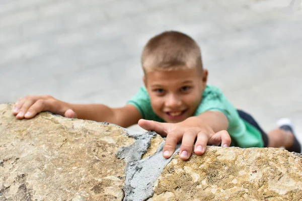 Um menino sobe uma montanha de pedra sem equipamento, uma subida perigosa. — Fotografia de Stock