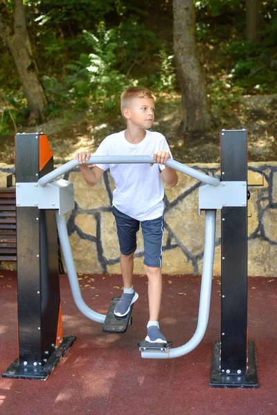 Chico ruso en la máquina de ejercicios al aire libre. el niño practica deportes regularmente. — Foto de Stock