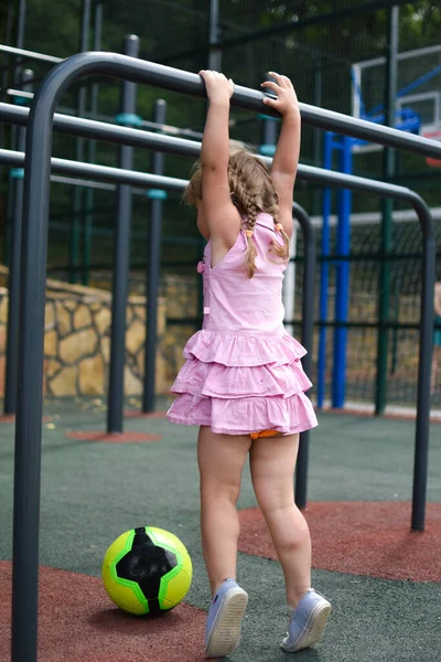 Little girl kid hangs on horizontal bar on outdoor sports ground. — Stock Image Little girl kid hangs on horizontal bar on outdoor sports ground. Royalty Free Stock Images