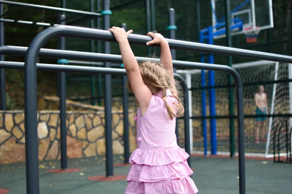 Little girl kid hangs on horizontal bar on outdoor sports ground. — Stock Image Little girl kid hangs on horizontal bar on outdoor sports ground. Stock Picture