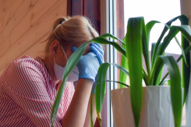 Tıbbi maskeli, eldivenli, yorgun bir kadın. Tıbbi kişi umutsuzluğa kapılmış durumda..