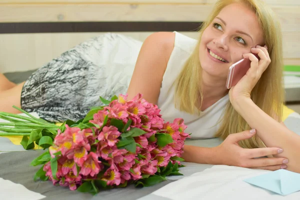 Молода красива жінка лежить на ліжку з букетом свіжих квітів . — стокове фото