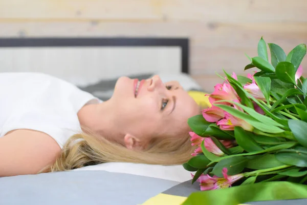 年轻漂亮的女人躺在床上，手里拿着一束鲜花. — 图库照片