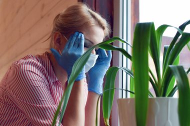 Baş ağrısı olan tıbbi maskeli bir kadın. Koronavirüsün ilk belirtileri..