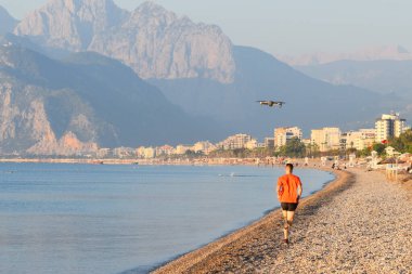 Genç adam kıyı boyunca koşar. Sabah sporcusu deniz kenarında koşuyor..