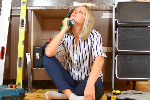 Una joven con un taladro en la mano. chica ama de casa hace reparaciones en el apartamento. — Foto de Stock