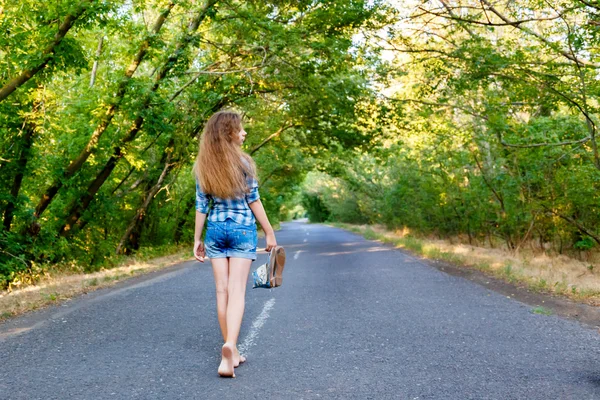 Красивая девушка в голубой клетчатой рубашке ходит по пустой дороге между — стоковое фото