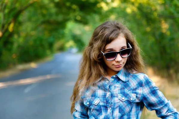 Krásná dívka v černé sluneční brýle na cestě mezi zelené — Stock fotografie