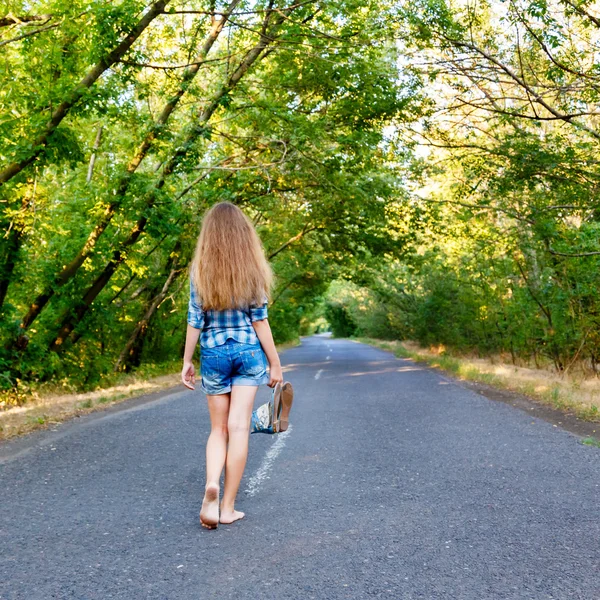 Красивая девушка ходит по пустой дороге между зелеными деревьями — стоковое фото
