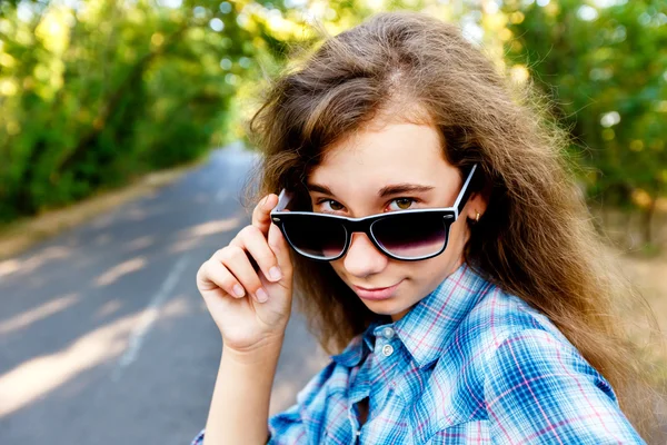 Krásná dívka v černé sluneční brýle na cestě mezi zelené — Stock fotografie