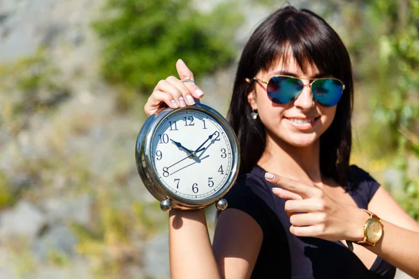 Belle fille dans un haut noir et des lunettes de soleil montrant une horloge. Fo Photos De Stock Libres De Droits