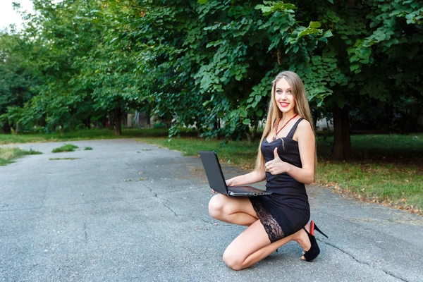 Sorrindo youg menina em vestido preto com laptop mostrando dedo para cima . — Fotografia de Stock