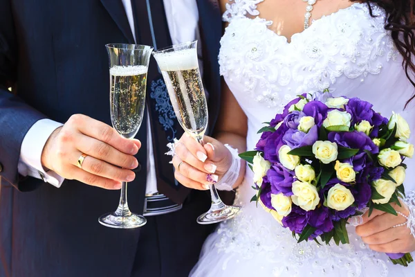 Braut und Bräutigam halten Champagnergläser und einen Brautstrauß in der Hand — Stockfoto