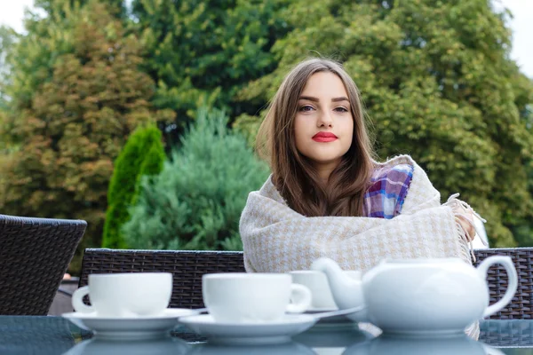 Menina sorridente bonita sentada à mesa em um café ao ar livre — Fotografia de Stock