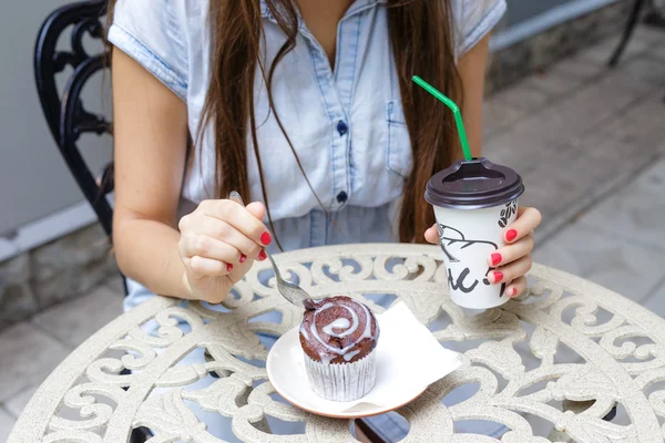 Mujer joven comiendo magdalena y beber café en la cafetería al aire libre — Foto de Stock