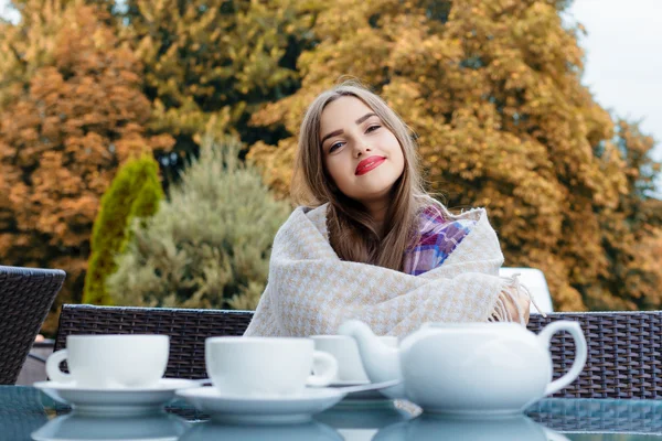 Hermosa chica sonriente envuelta en una manta sentada al aire libre —  Fotos de Stock