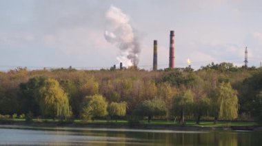 Orman ve nehir yakınlarındaki fabrika borularının dumanı. Ağır sanayi tesislerinin hava ve doğa kirliliği küresel çevre sorunu.