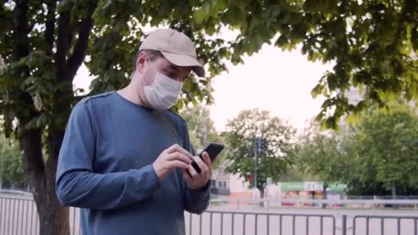 Man i skyddsmask gå på en gata, med hjälp av internet på smarttelefon. — Stockvideo