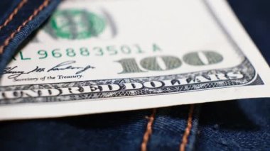 100 Amerikan Doları banknotu dönen masanın üzerindeki kot pantolonun cebinde. Aşırı yakın plan, Yüzeyin Sığ Derinliği. İş konsepti.