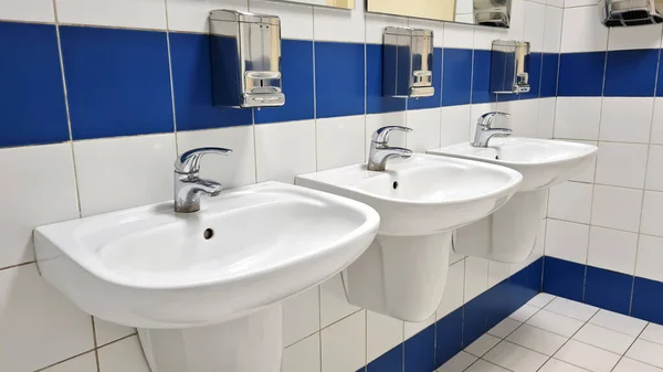 3 white porcelain wash basins in public restroom at shopping mall.