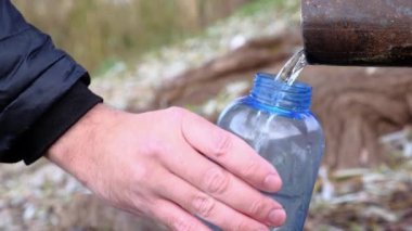 Yürüyüş yapan bir adam parktaki mavi plastik bir şişeye kaynak suyu döküyor. Yakın plan el..