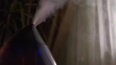 Karanlık odadaki modern hava nemlendiricisinden buhar çıkıyor. Yakın plan, insan yok..