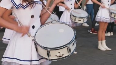 Beyaz denizci kısa elbiseli genç bayanlar yaz günü bir geçit töreninde davul çalarlar. Festivalde belediye orkestrasının bateristleri sahne alacak. Tahta sopalarla yakın plan çekilen eller..