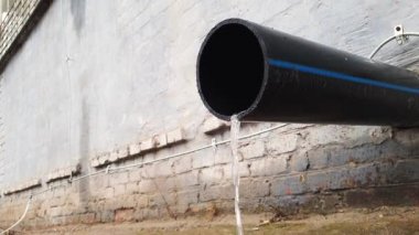 Yağmurdan sonraki gün endüstriyel bir binadaki siyah plastik drenaj borusundan su akışı.