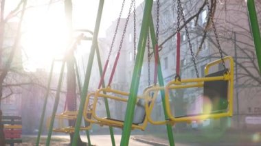 Güneşli bir yaz sabahında, şehrin çocuk parkında boş salıncaklar. Gün doğumu, arka ışık, insan yok..