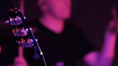 Bulanık davulcu kulüp sahnesinde davul çalıyor. Odaklanan akuistik gitar yakasının bir parçası.