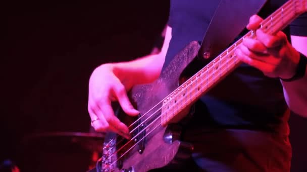 클럽에서 록 콘서트에서 일렉트릭 베이스 기타를 연주하는 남성 기타리스트. 붉은 조명, 손을 감는 모습. — 비디오