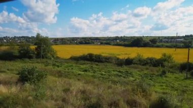 Hızlı giden trenin açık penceresinden kırsal sarı tarlalara bakın. Kırsal yaz çayırlarında güneşli yaz gününde mavi bulutlu bir arka planda.