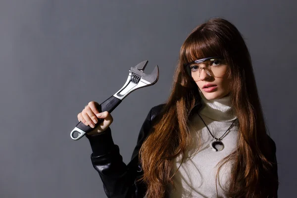 Chica en gafas de seguridad con llave ajustable en un fondo oscuro —  Fotos de Stock