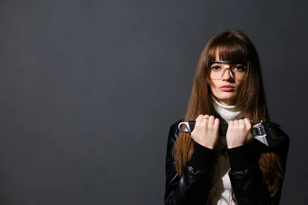 Chica en gafas de seguridad con llave ajustable en una pared oscura bac —  Fotos de Stock