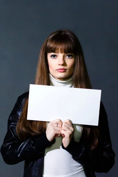 Chica con la tarjeta vacía blanca en blanco sobre un fondo de pared oscura — Foto de Stock