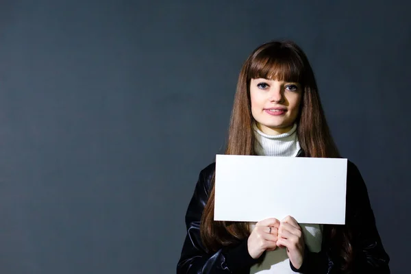 Genç kadın tutan bir karanlık duvar backgr üzerinde beyaz boş kartı boş — Stok fotoğraf
