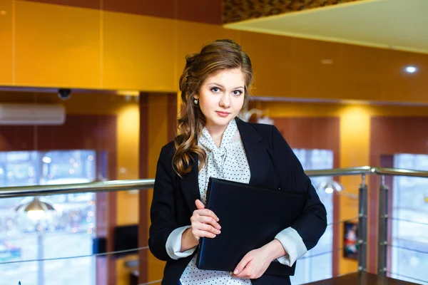 Krásná mladá dívka stojící v kanceláři a držení notebooku — Stock fotografie