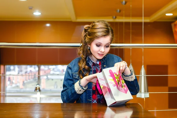 Piękna dziewczyna w kawiarni patrząc w worku prezent — Zdjęcie stockowe