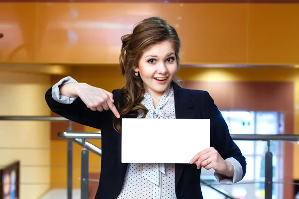 Genç güzel kadın gülümseyerek boş beyaz kartında gösterir — Stok fotoğraf