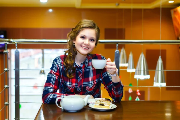 Sonriente hermosa chica en una camisa a cuadros beber té en un café — Foto de Stock