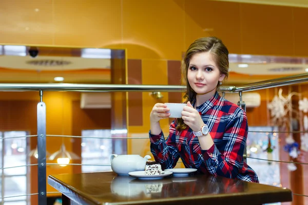 Joven chica agradable en una camisa a cuadros beber té en un café — Foto de Stock