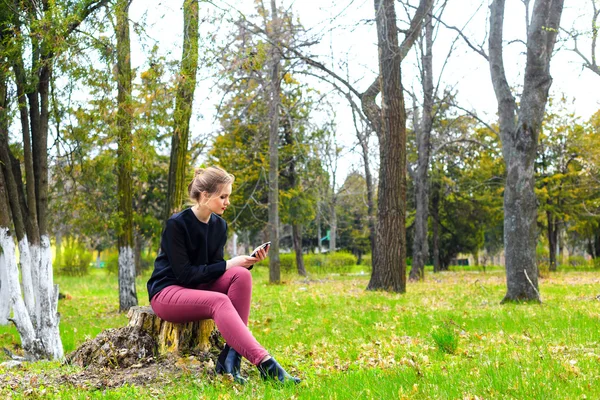 Mooi Meisje Zit Een Boomstronk Het Park Met Smartphone — Stockfoto