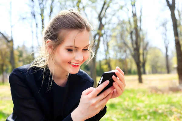 Chica feliz con el pelo despeinado mirando en el teléfono inteligente sonriendo —  Fotos de Stock