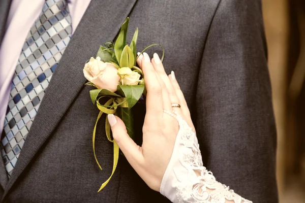 Hang of a bride adjusting boutonniere on grooms jacket — Stock Photo, Image