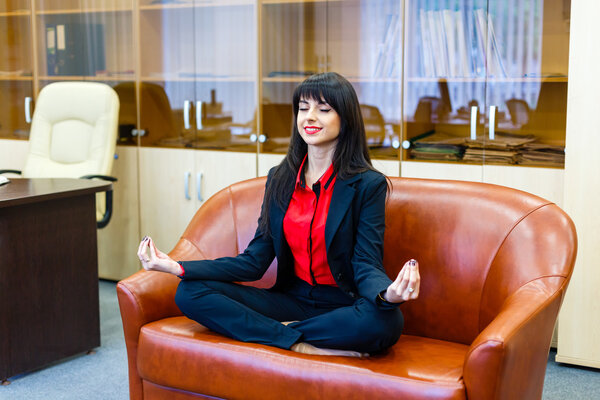 Nice smiling businesswoman sitting on a sofa in the lotus positi