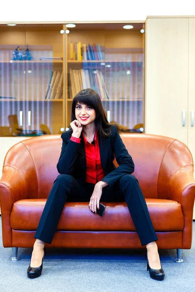 Beautiful smiling girl in a suit sitting in an office on the cou — Stock Photo, Image