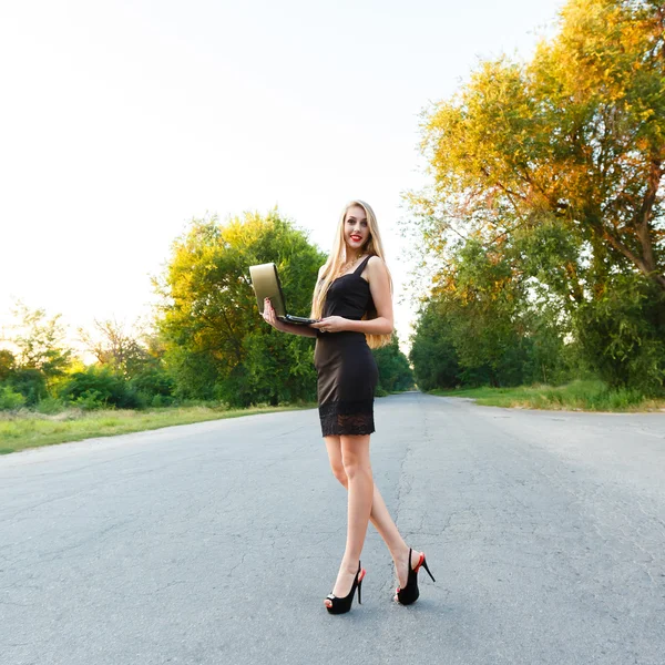 Joven hermosa mujer sonriente con un ordenador portátil en el camino —  Fotos de Stock