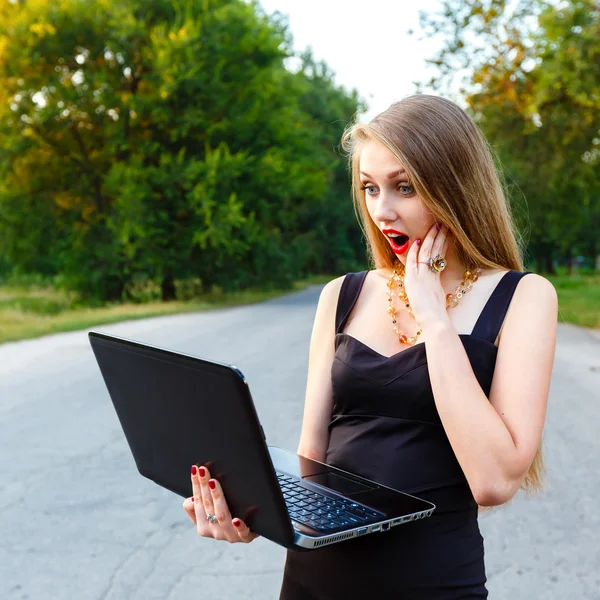 Hermosa chica mira a un ordenador portátil, mientras que en el camino —  Fotos de Stock